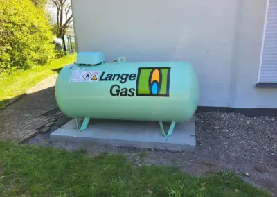 Türkis-grüner Flüssiggastank von Langner Gas mit Sicherheitskennzeichnung an der Außenwand, auf betoniertem Fundament neben Zaun und Rasen im Tageslicht.